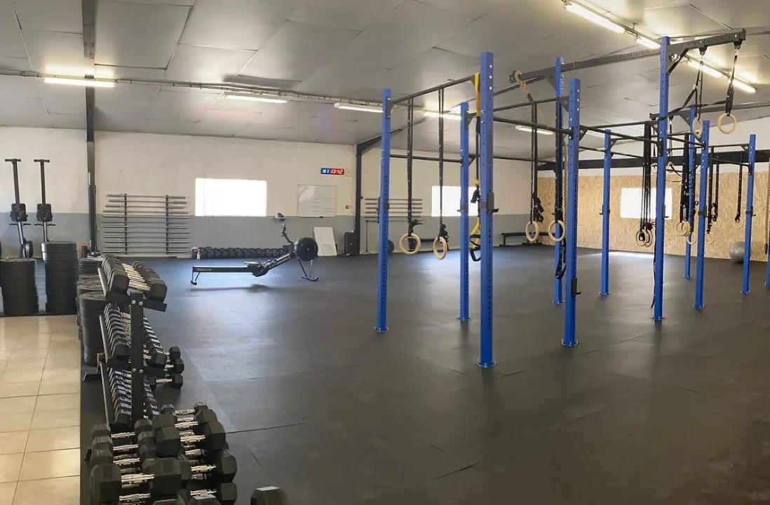Salle de CrossFit vue d’ensemble avec structures bleues, anneaux, rameur et rack d’haltères