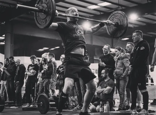Athlète soulevant une barre chargée devant des spectateurs lors d’une épreuve de CrossFit